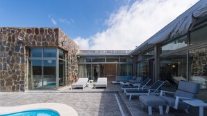 A modern outdoor pool area with stone walls, glass doors, and lounge chairs. - Villa in Anfi Tauro near Beach & Golf (Mogán)