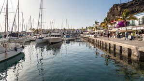 A marina with multiple boats docked, a pier with people walking, and buildings with shops and restaurants. - Apartment in Mogán Playa near the Beach (Mogán)