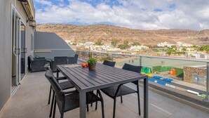 An outdoor patio with a table and chairs, overlooking a tennis court and a hilly landscape. - Apartment in Mogán Playa near the Beach (Mogán)