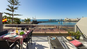 Een terras met een eettafel, met uitzicht op een strand en een jachthaven.