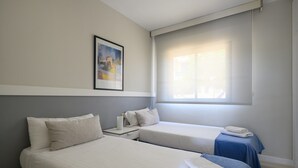 Ein Hotelzimmer mit zwei Betten, einem Nachttisch, einem gerahmten Bild an der Wand und einem Fenster mit Vorhängen.