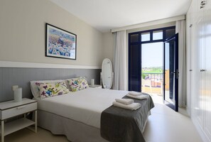 Ein Hotelzimmer mit einem großen Bett, einem Nachttisch mit Lampe, einem Spiegel und Blick ins Freie durch eine offene Tür.