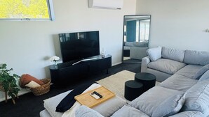 Una sala moderna con un amplio sofá seccional gris, un televisor de pantalla plana, una mesita auxiliar negra y un espejo grande en la pared.