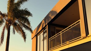 Un edificio moderno con balcón, ventanas amplias y una palmera.