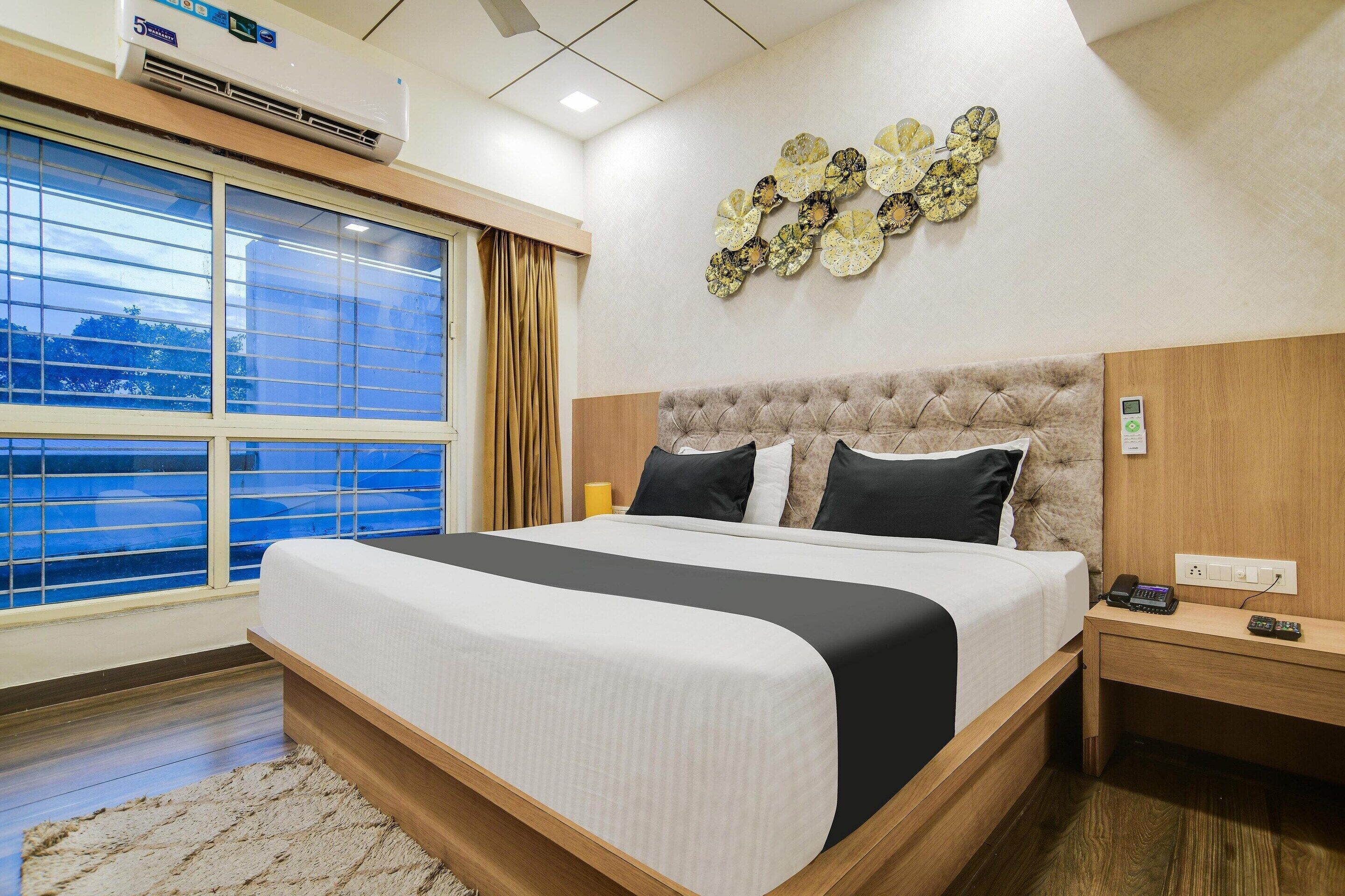A hotel room with a large bed, a bedside table with a phone, a wall clock, and a window with curtains.