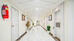 Ein Hotelgang mit weißen Marmorböden, einem an der Wand befestigten Feuerlöscher, Blumentöpfen und gerahmten Kunstwerken.