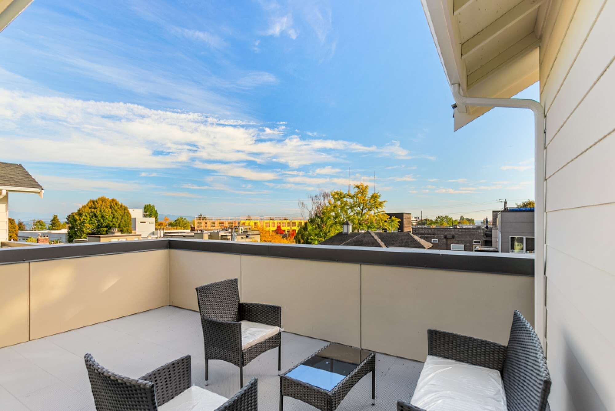 Terraço no telhado com móveis de vime, uma mesa pequena e vista para a paisagem urbana.