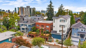 Un quartier résidentiel avec des maisons modernes, un mélange de bâtiments à un ou plusieurs étages, et une vue sur les gratte-ciel de la ville en arrière-plan.