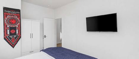 A bedroom with a bed, a TV mounted on the wall, and a door leading to another room.