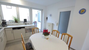 A small, clean kitchen with white cabinets, a dining table with a white tablecloth, and a potted plant on the windowsill.