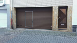 A building with a large garage door, a small door with a number, and a metal gate.