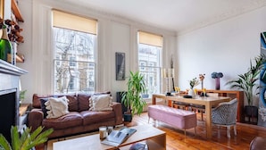 A spacious living room with a brown leather sofa, a wooden coffee table, and a dining area with a wooden table and chairs.