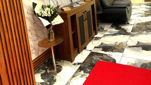 A modern living room with a marble wall, a flat-screen TV, a wooden console, a black leather sofa, and a red carpet. - NERA OTEL (Istanbul)