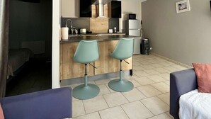 A compact living space with a kitchenette, two bar stools, a bed, and a sofa.