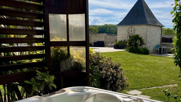A hot tub in a covered outdoor area with a view of a stone building and a grassy yard.