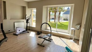 A spacious room with a large window, a standing bike, a rowing machine, and a small exercise bench.