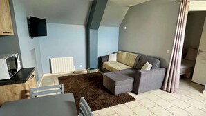 A compact living space with a dining area, a sofa, and a television mounted on the wall.
