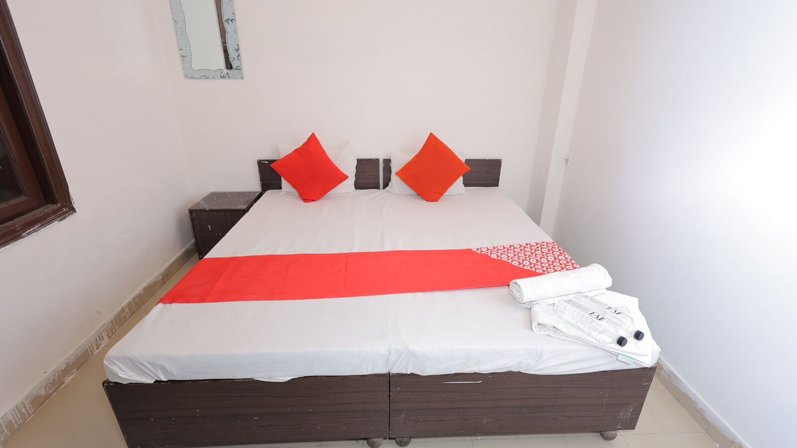 Una cama bien hecha con una colcha blanca y roja, dos almohadas rojas y una toalla blanca doblada al lado.
