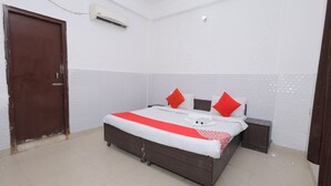 A bedroom with a bed, two nightstands, a brown door, and a white air conditioning unit on the wall. - Hotel ZoVo Agra (Agra)
