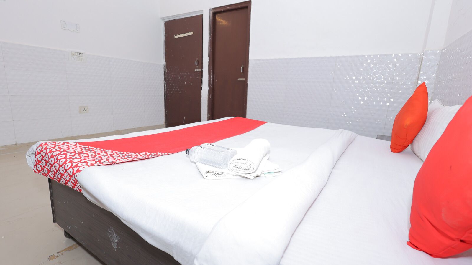 A hotel room with a bed, a red and white patterned bedspread, a white pillow, and a red pillow.