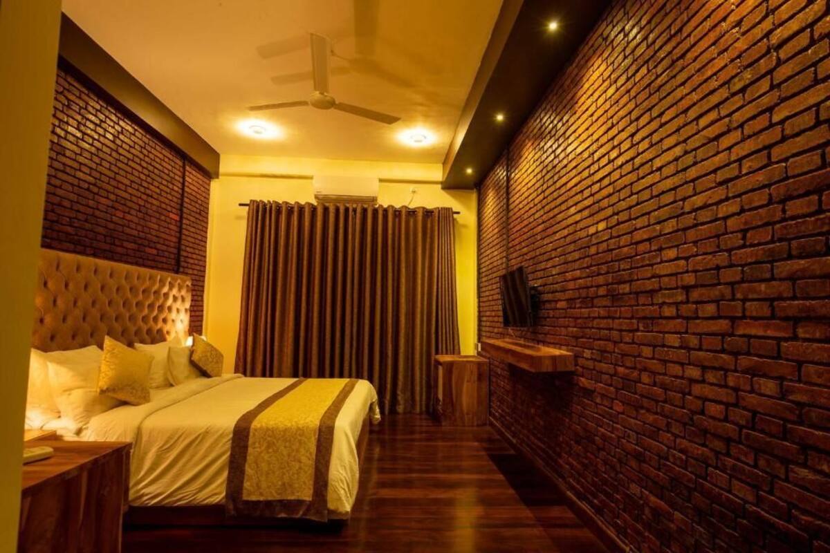A bedroom with a brick wall, a tufted headboard, a bed with white bedding, a ceiling fan, and a small wooden side table.