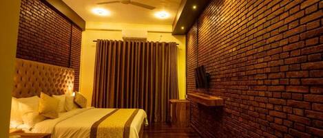 A bedroom with a brick wall, a tufted headboard, a bed with white bedding, a ceiling fan, and a small wooden side table.