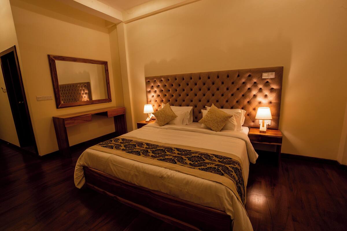 A hotel room with a large bed, two bedside tables with lamps, a mirror on the wall, and a wooden headboard.