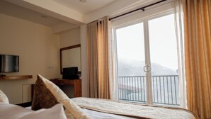 A hotel room with a bed, a television, a desk, and a large window with curtains. - Manthra Leisure (Kandy)