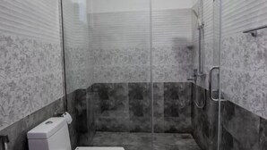 A compact bathroom with a toilet, shower, and glass door. - Manthra Leisure (Kandy)