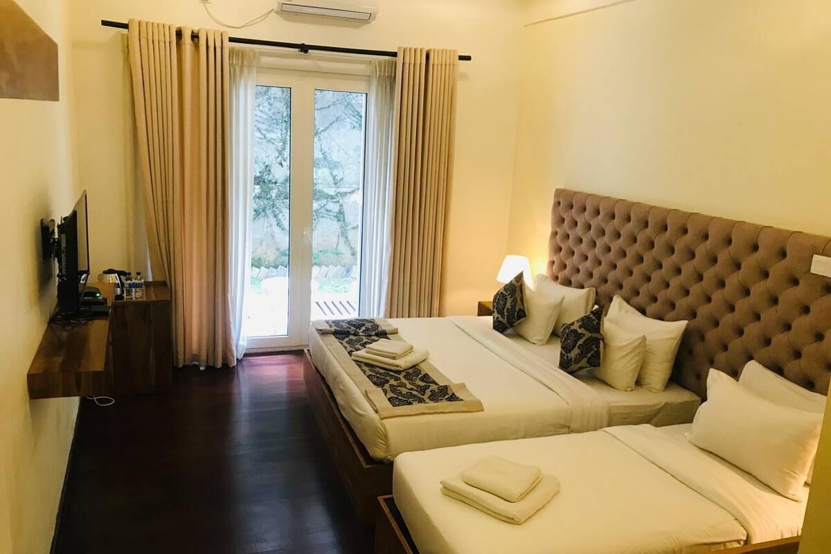 A hotel room with two beds, a TV, a desk, and a view of the outdoors.