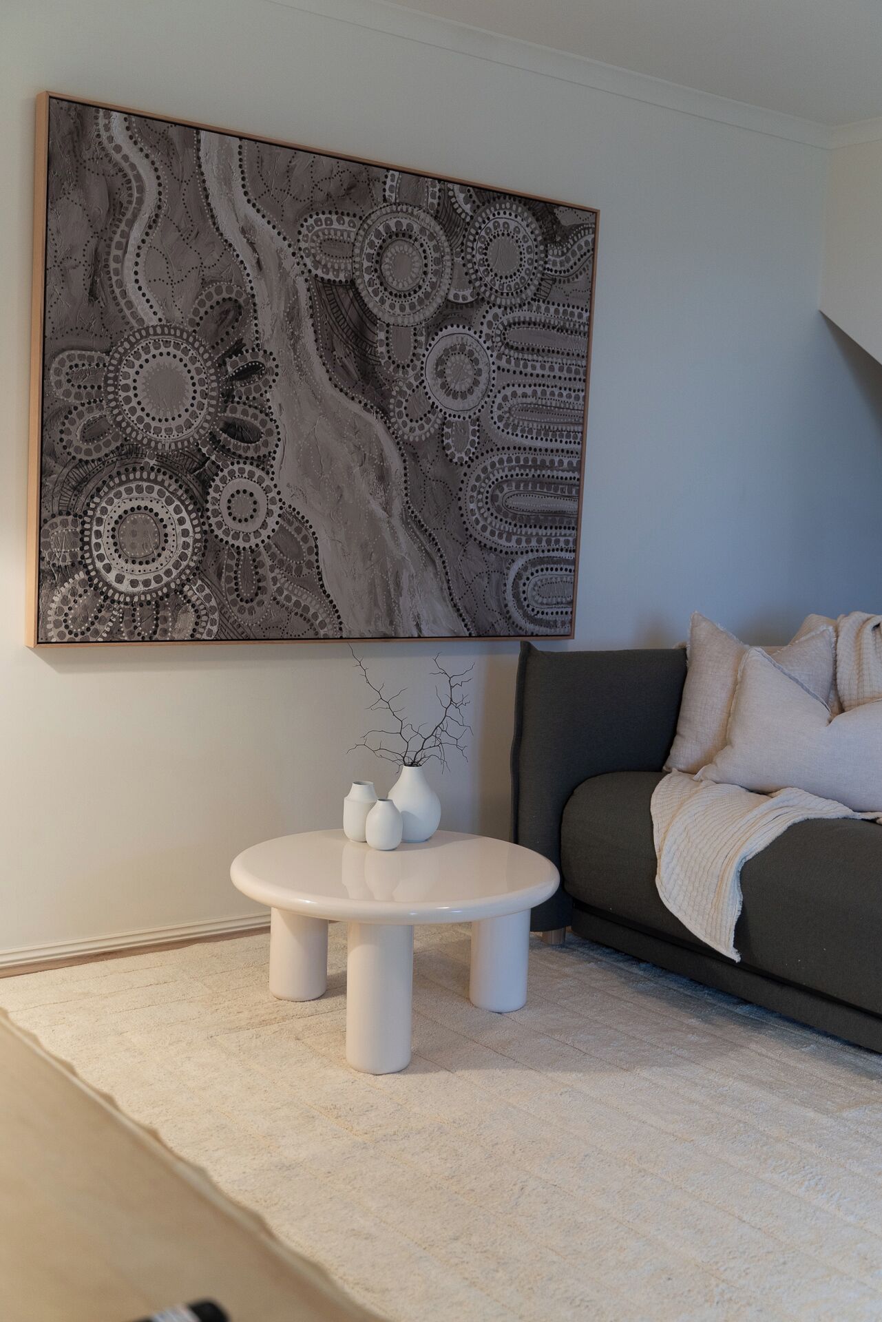 A modern living room with a round white coffee table, a gray sofa, and a large abstract painting on the wall.
