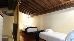 Une petite pièce chaleureuse avec deux lits, des poutres en bois au plafond et un escalier menant à un autre espace.