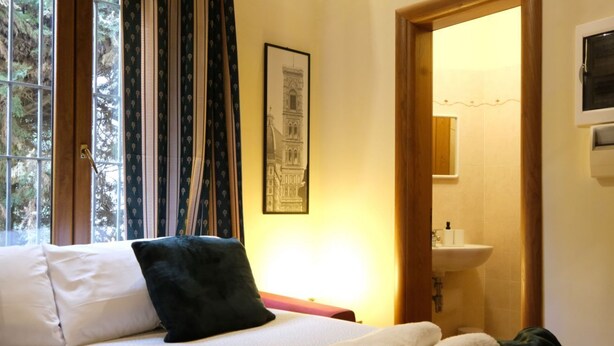 Une chambre à coucher avec un lit, des oreillers, un tableau encadré, une fenêtre avec des rideaux et une vue sur une salle de bain.