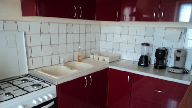 Une cuisine avec des meubles de couleur rouge, une cuisinière blanche et un dosseret carrelé.