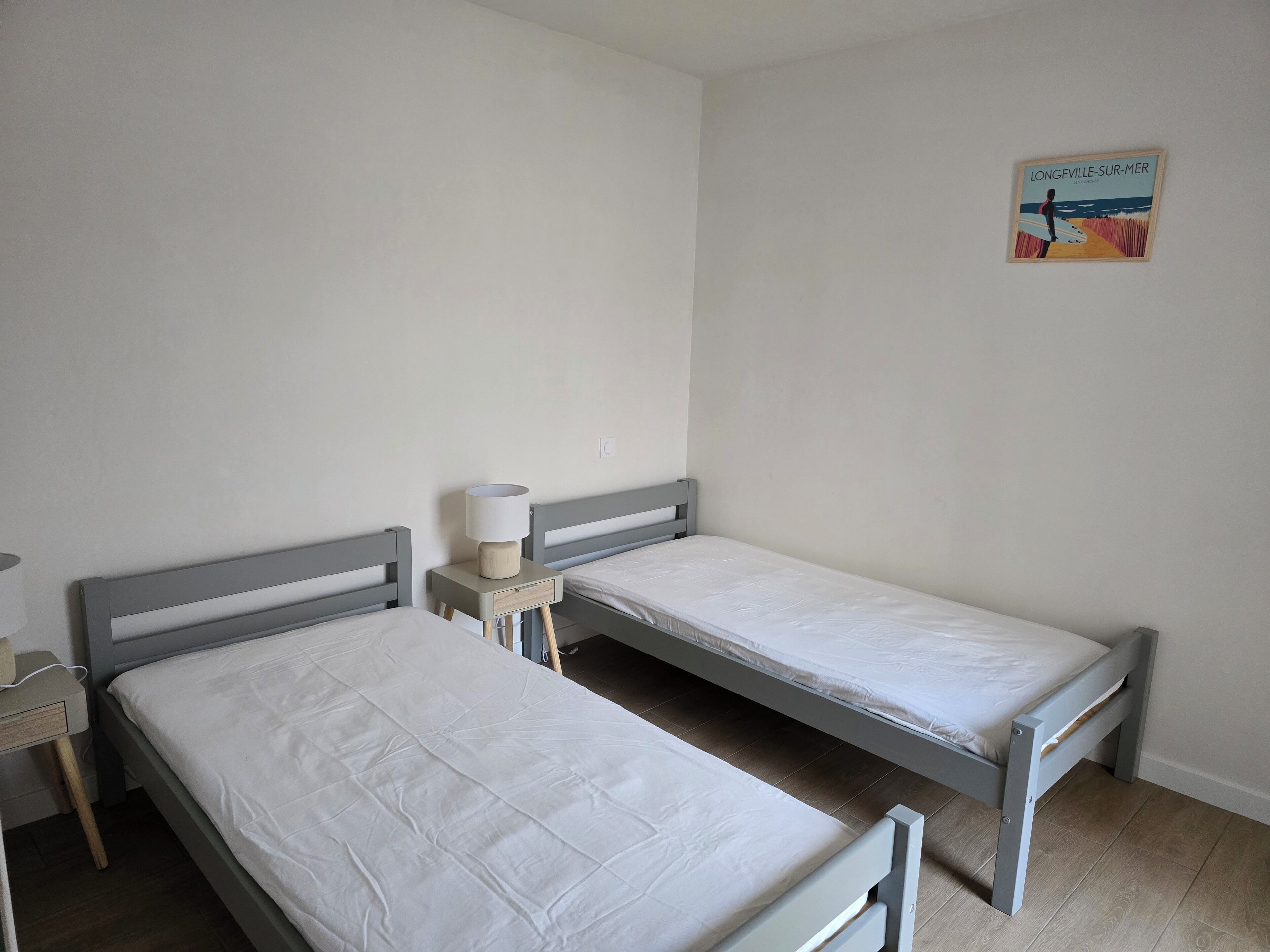 Une chambre avec deux lits simples, une table de chevet avec une lampe et un tableau accroché au mur.