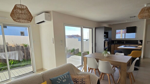 Een moderne woonkamer met een bank, een eettafel en stoelen. Er is een schuifdeur naar een balkon.