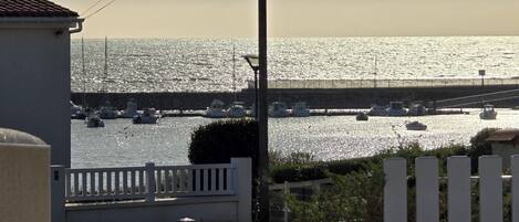 Vista costera con un puerto deportivo, barcos y una cerca blanca.