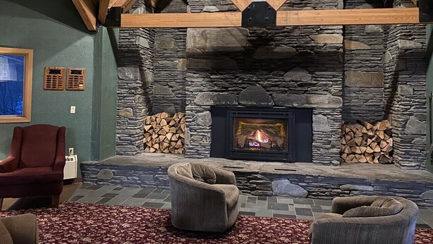 A stone fireplace with a fire, wooden beams, and two armchairs in a cozy room.