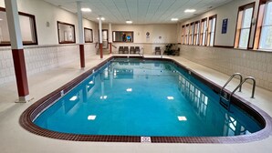 An indoor swimming pool with a tiled border, a no diving sign, and a seating area with chairs and a small table.