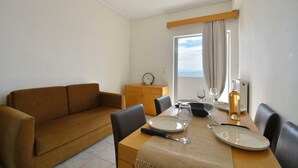 A dining area with a wooden table set for two, a sofa, and a small cabinet. - Sunrise (Corfu)