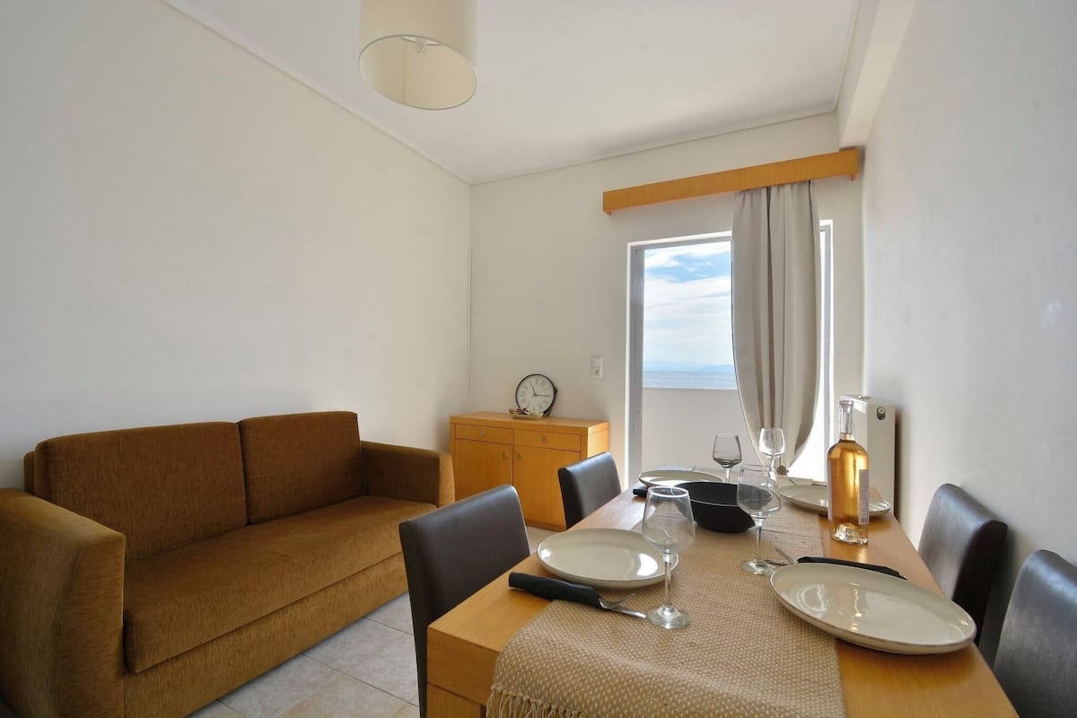 Uma área de jantar com uma mesa de madeira posta para dois, um sofá e um pequeno armário.