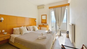 A hotel room with a large bed, a bedside table with a lamp, a small table with a mirror, and a view of the sea through a window with curtains. - Sunrise (Corfu)