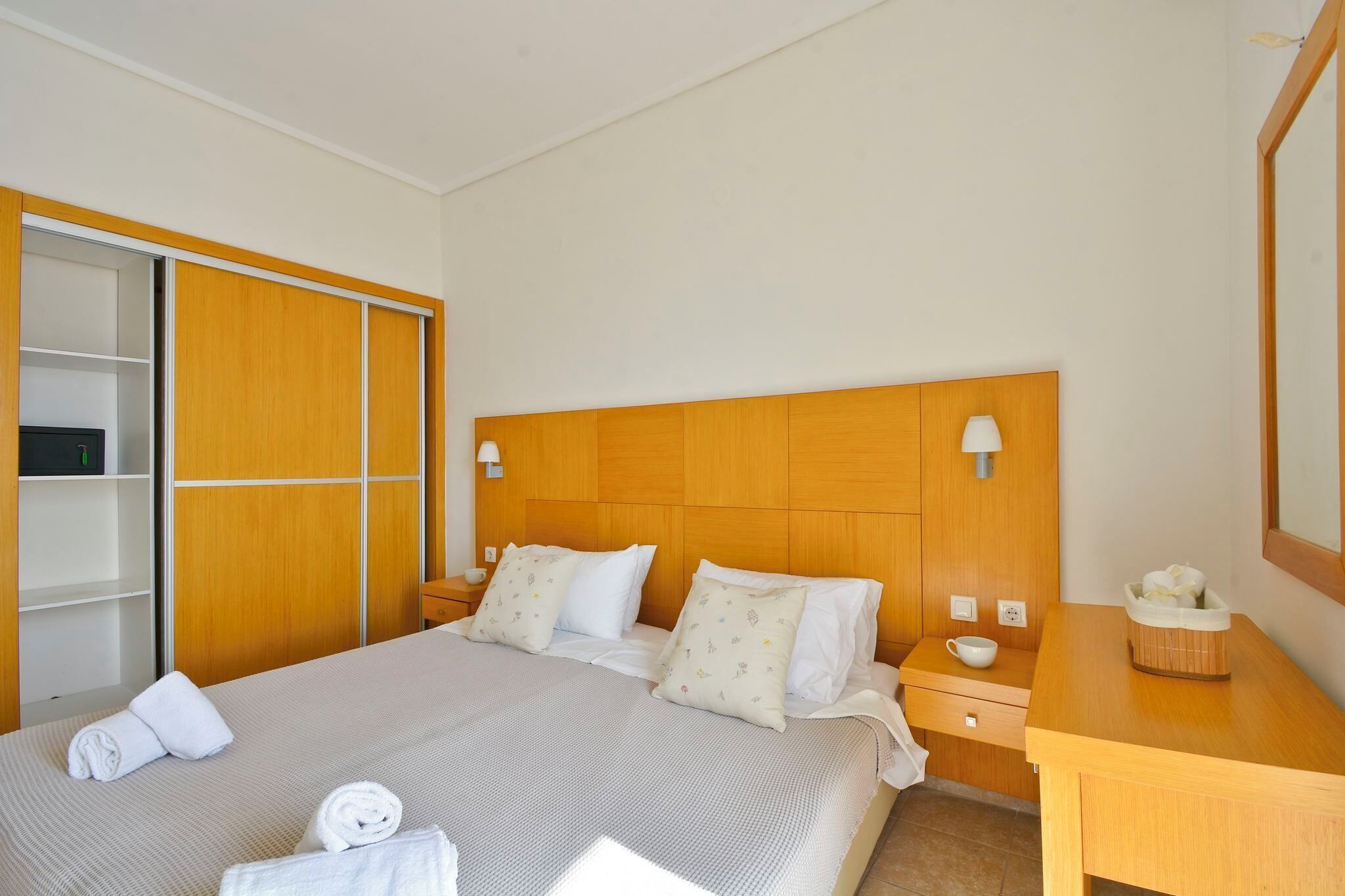 A hotel room with a large bed, wooden headboard, bedside tables, a nightstand, a wooden desk, and a wardrobe.