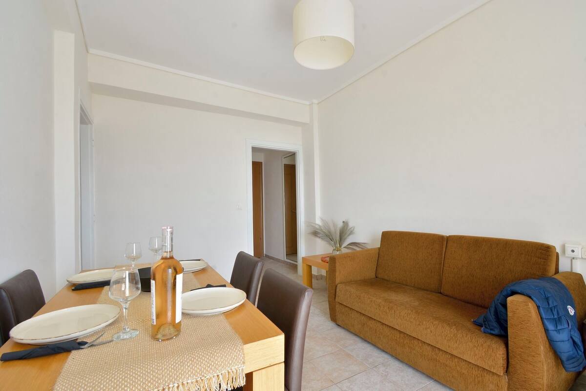Uma área de refeições com uma mesa posta para dois, um sofá e uma luminária.