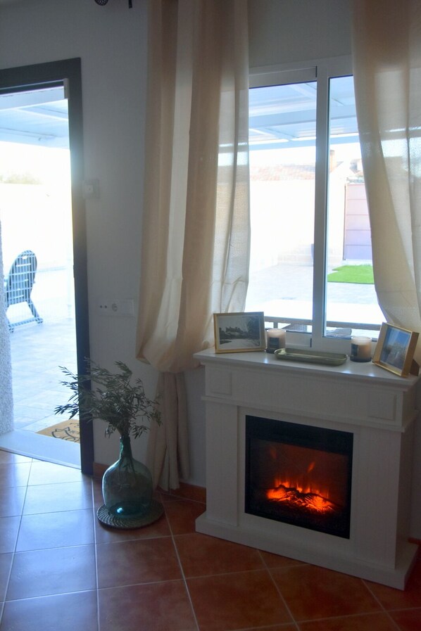 A room with a fireplace, a window with curtains, a vase with plants, and a door leading outside. - Resting place with swimming pool, garden, BBKA. Fluvial Beach. Toledo and Puy Du Fou (CM)