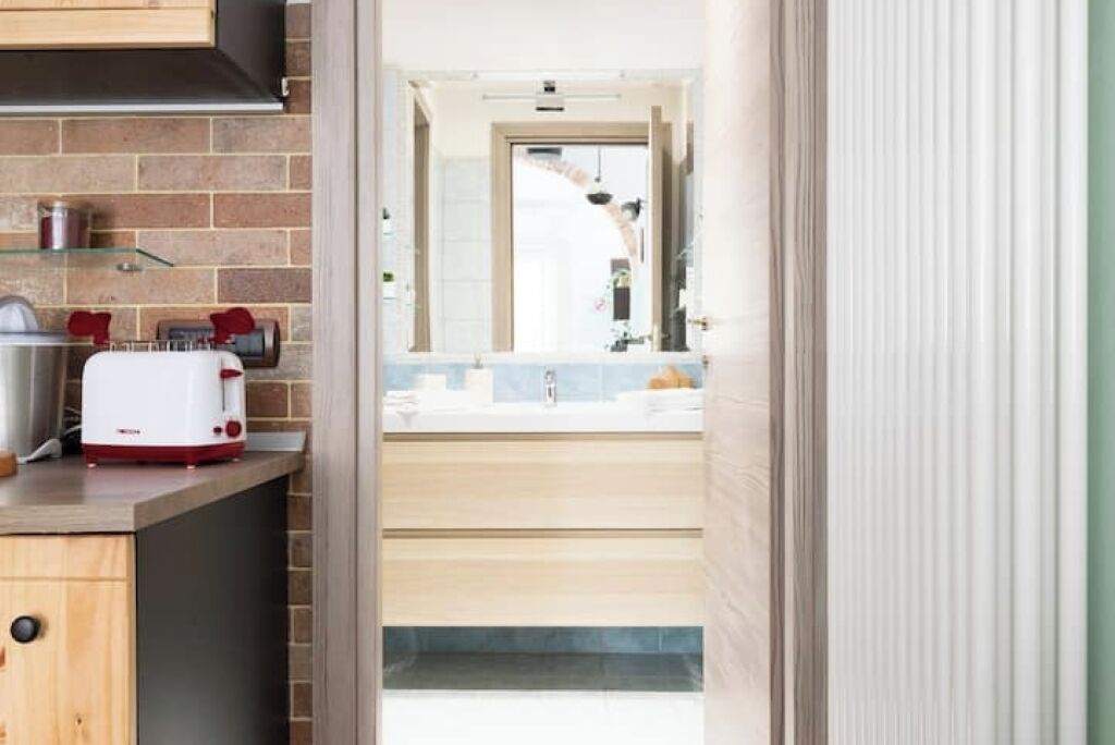 A modern kitchen with a toaster, a sink, and a window overlooking a bathroom.