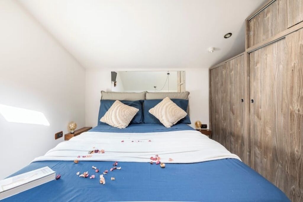 Una camera da letto con un letto, cuscini, un armadio e un comodino con una lampada.