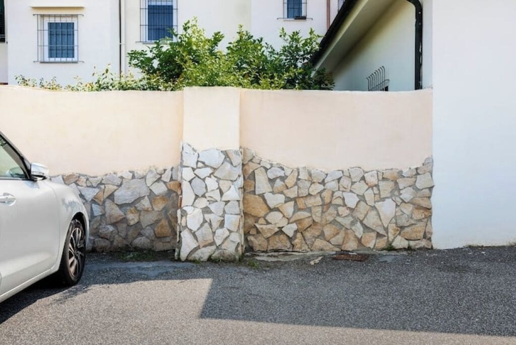 A white car parked next to a stone wall with a building in the background.