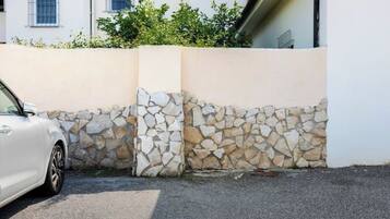 A white car parked next to a stone wall with a building in the background.