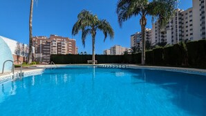 A swimming pool with clear blue water, surrounded by palm trees and modern apartment buildings. - BULEVAR rooftop apartment (La Vila Joiosa)